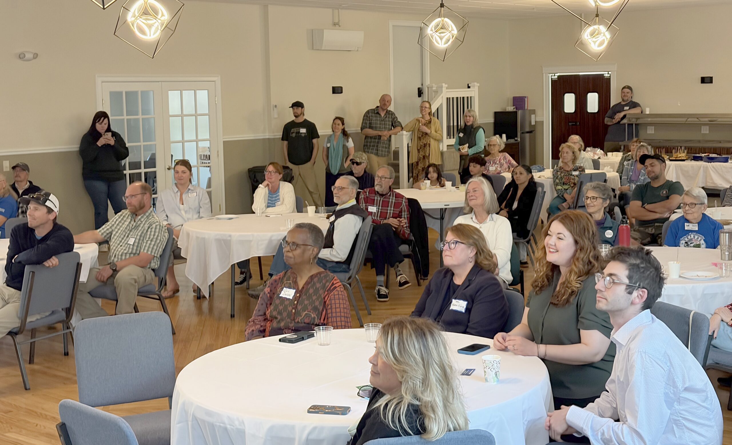A crowd sitting at tables listens to Beth Bosworth speak